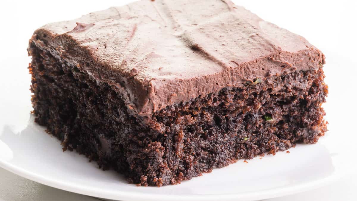 A slice of vegan chocolate cake with glazed zucchini on a white plate.