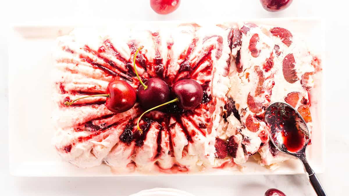 An overhead photo of a cherry semifreddo topped with cherry jam and fresh cherries and a jam-covered spoon.