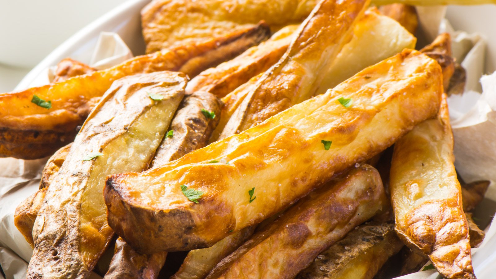 Close-up of French fries on a plate. They are golden brown with flecks of fresh herbs on top.