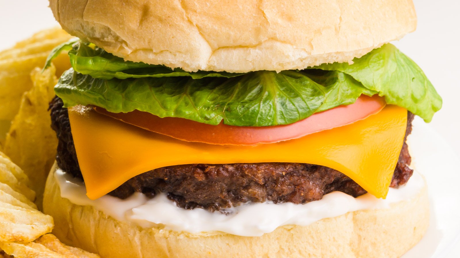 Close-up of a burger on a bun with cheese, tomatoes and lettuce on top. On the plate there are French fries.