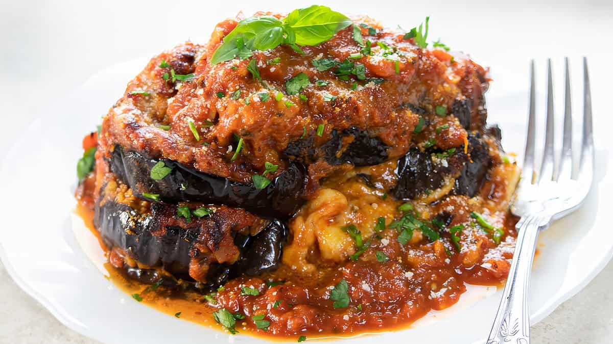 Baked eggplant parmesan on a white plate topped with fresh basil