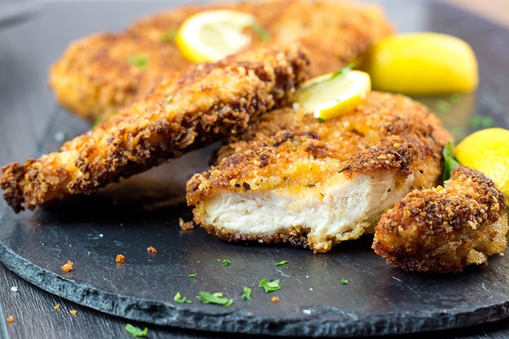 Crispy breaded chicken cutlets on a plate with a cut piece showing the juicy meat