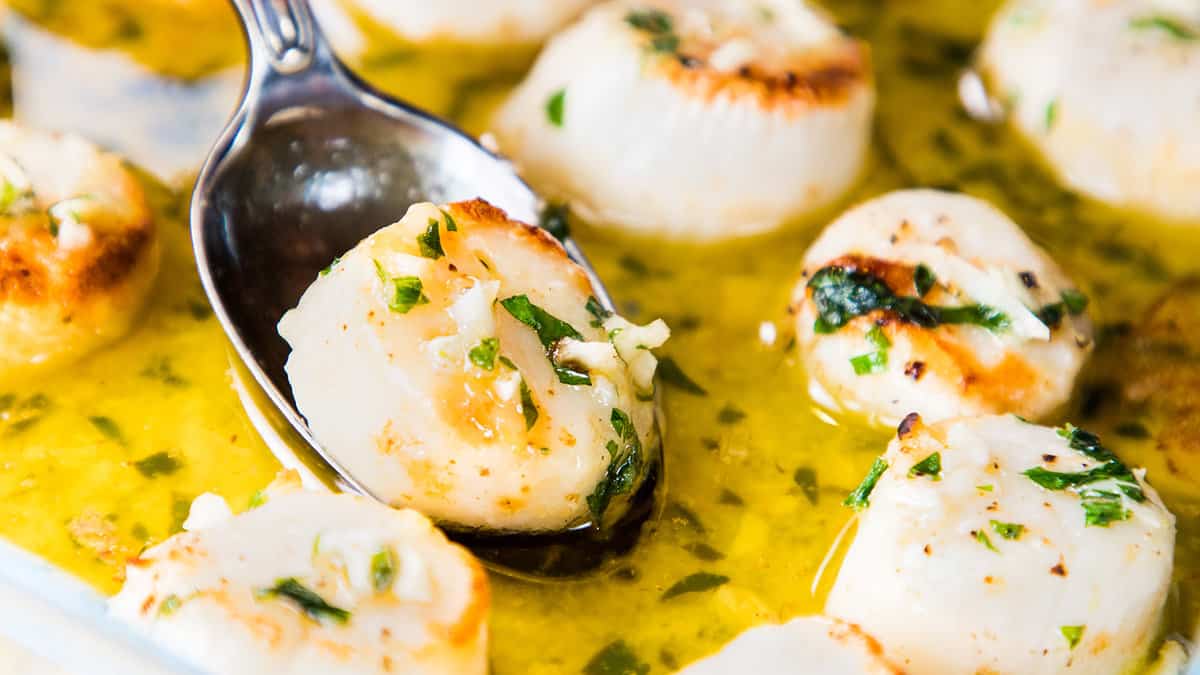 Grilled scallops in garlic butter sauce served with a spoon.