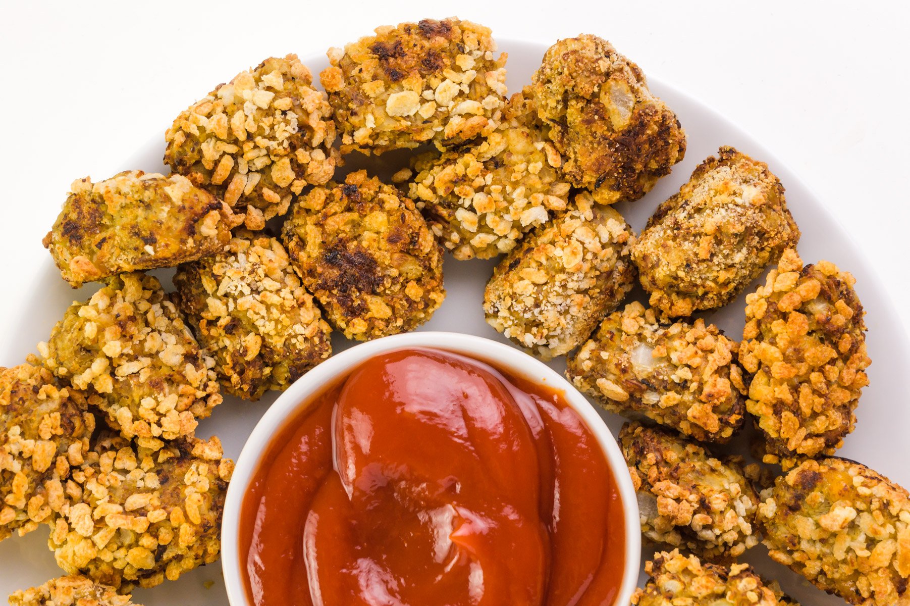 Looking down at a plate of cauliflower tater tots next to a bowl of ketchup.