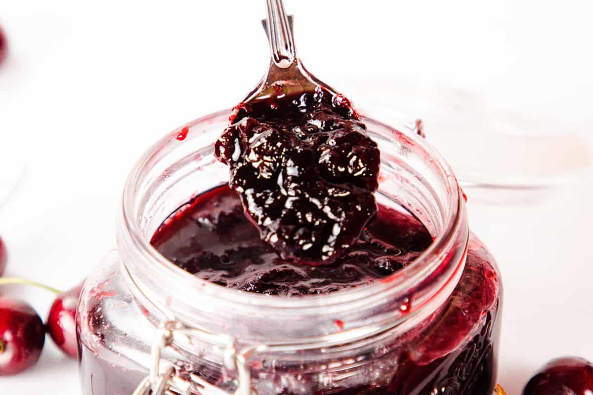 A spoon with cherry jam on the full jar