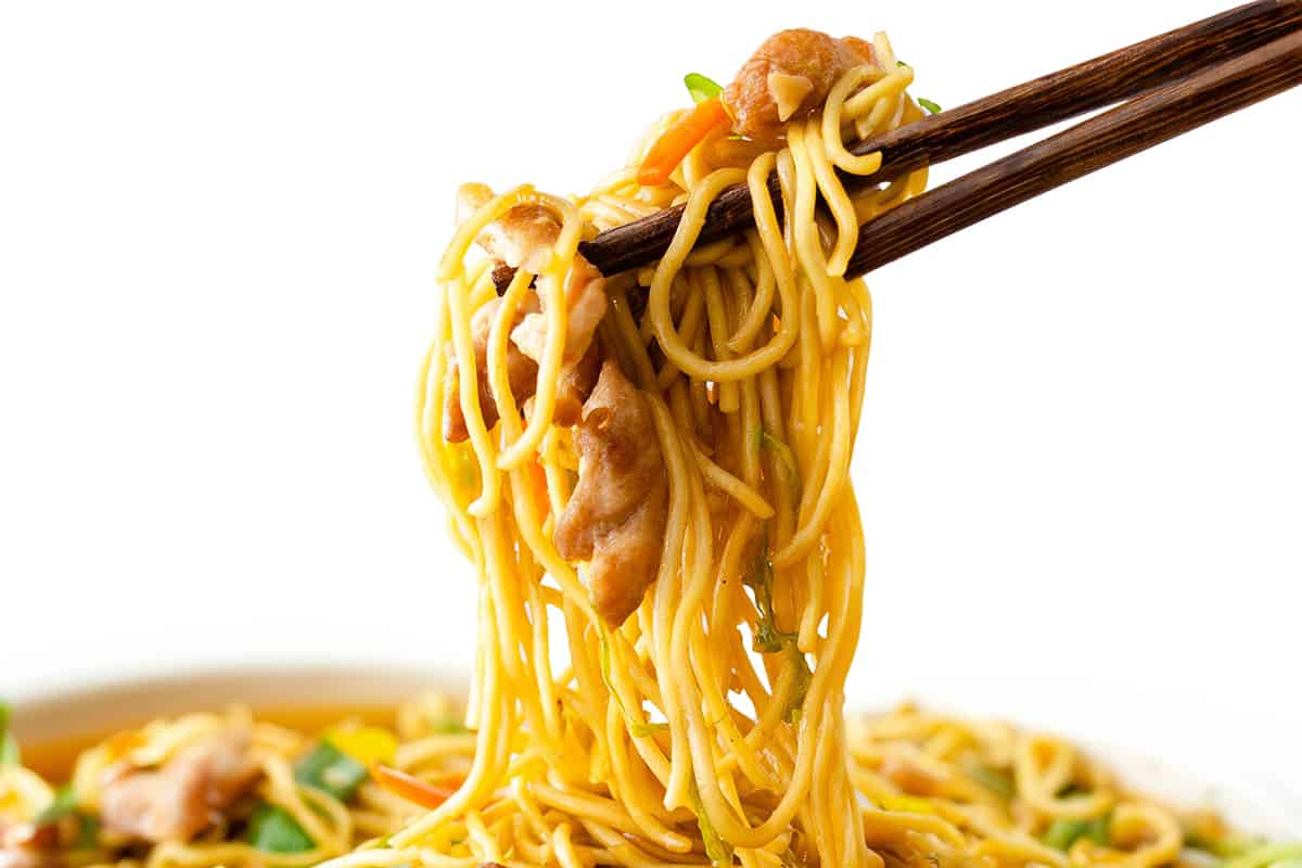 Chopsticks holding a chicken lo mein with noodles, vegetables and chicken, on a white background.