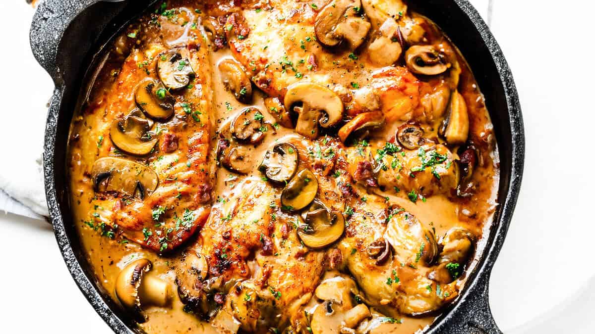 A close up image of a cast iron skillet filled with chicken marsala and mushrooms.