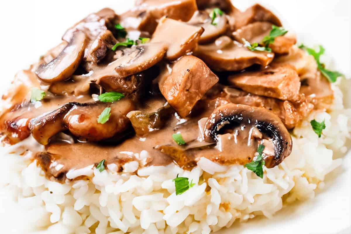 A close up image of a chicken stroganoff on a white plate with a white background.