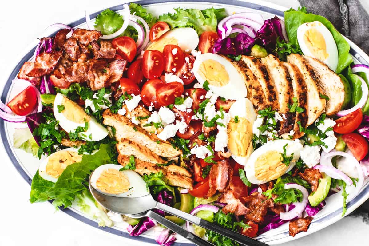 An overhead photo of a corn cob salad layered with eggs, bacon, tomatoes, lettuce, etc.