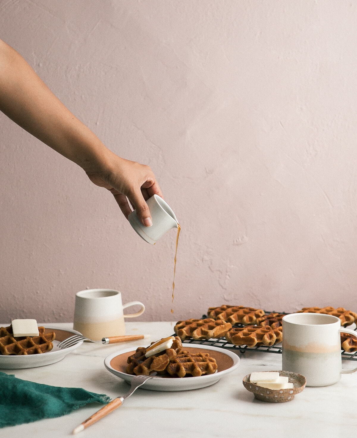 Hand-pouring syrup over a plate of crispy pumpkin waffles.