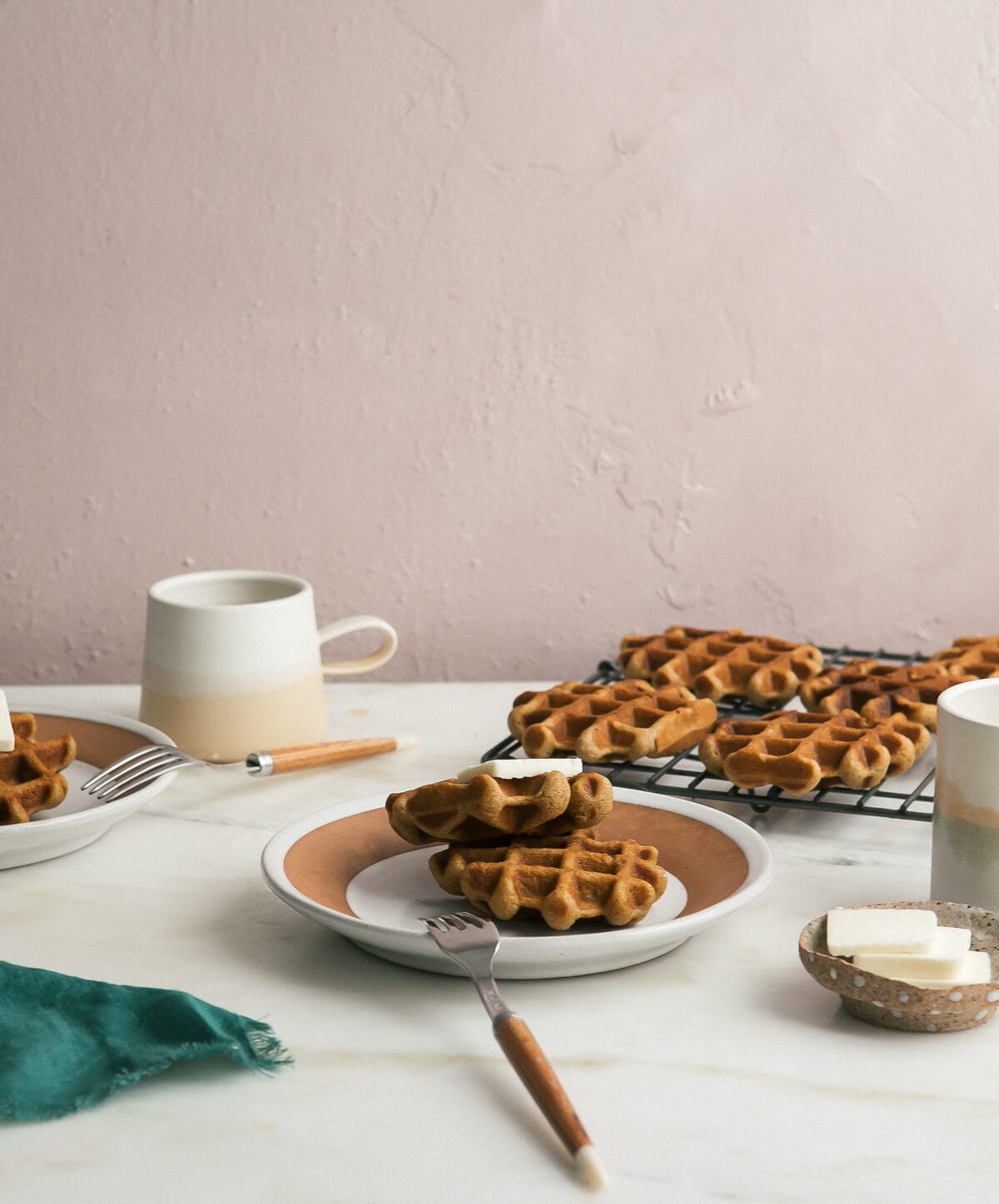 Crispy pumpkin waffles stacked on a plate topped with butter.