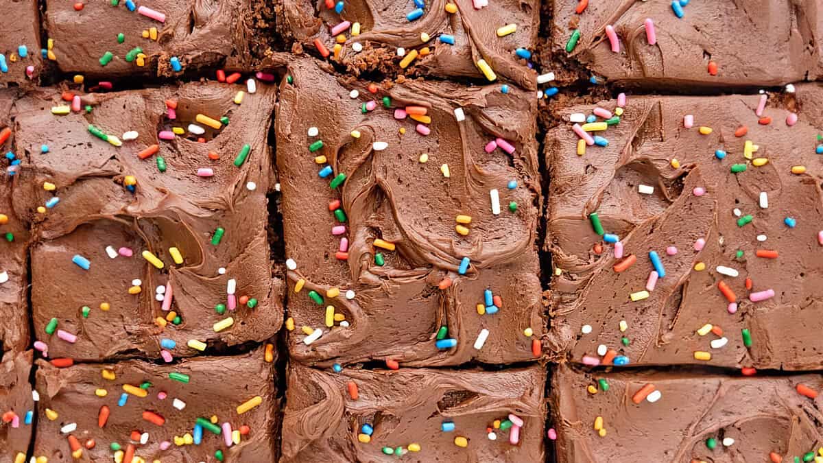 A close up image of a sliced ​​cake with chocolate frosting and sprinkles.