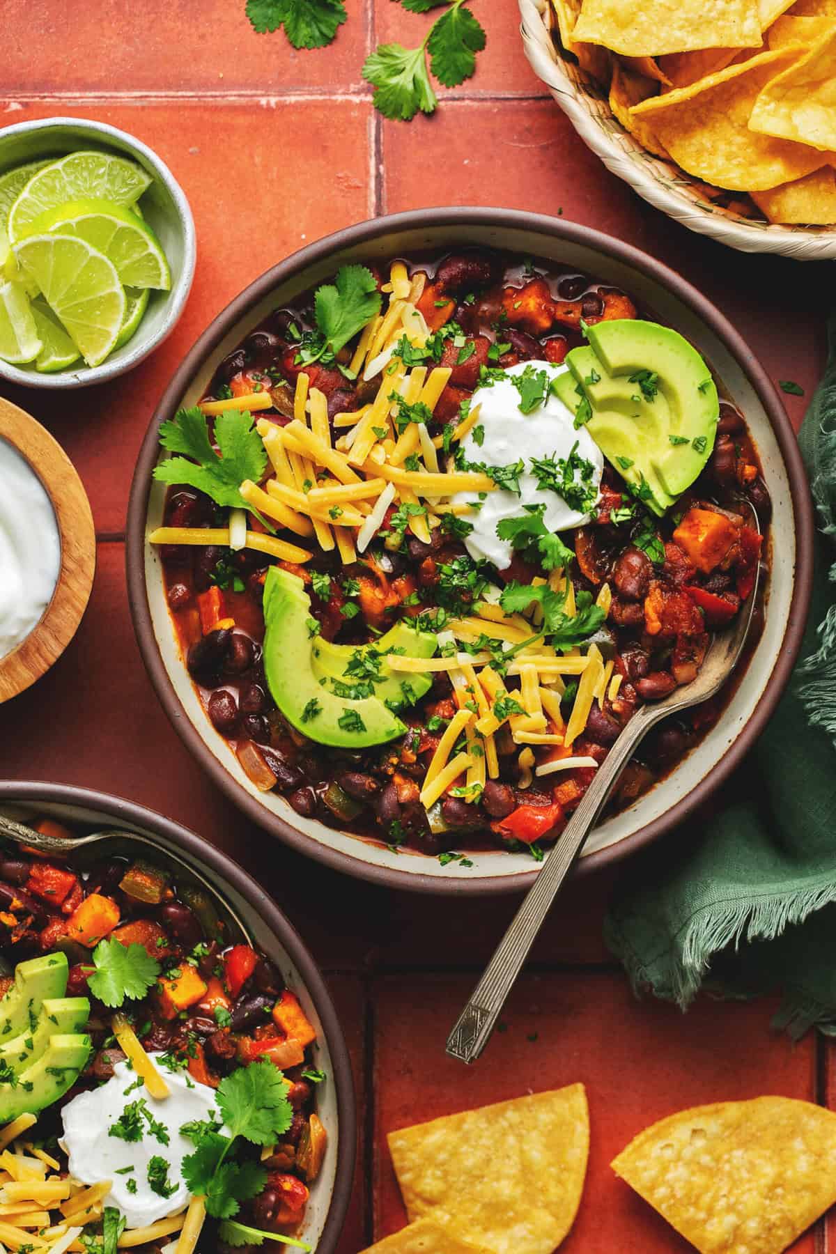 Two bowls of chili with cheese, avocado and sour cream toppings.