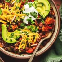 Overhead view of a bowl of chili with toppings and a spoon in a bowl.