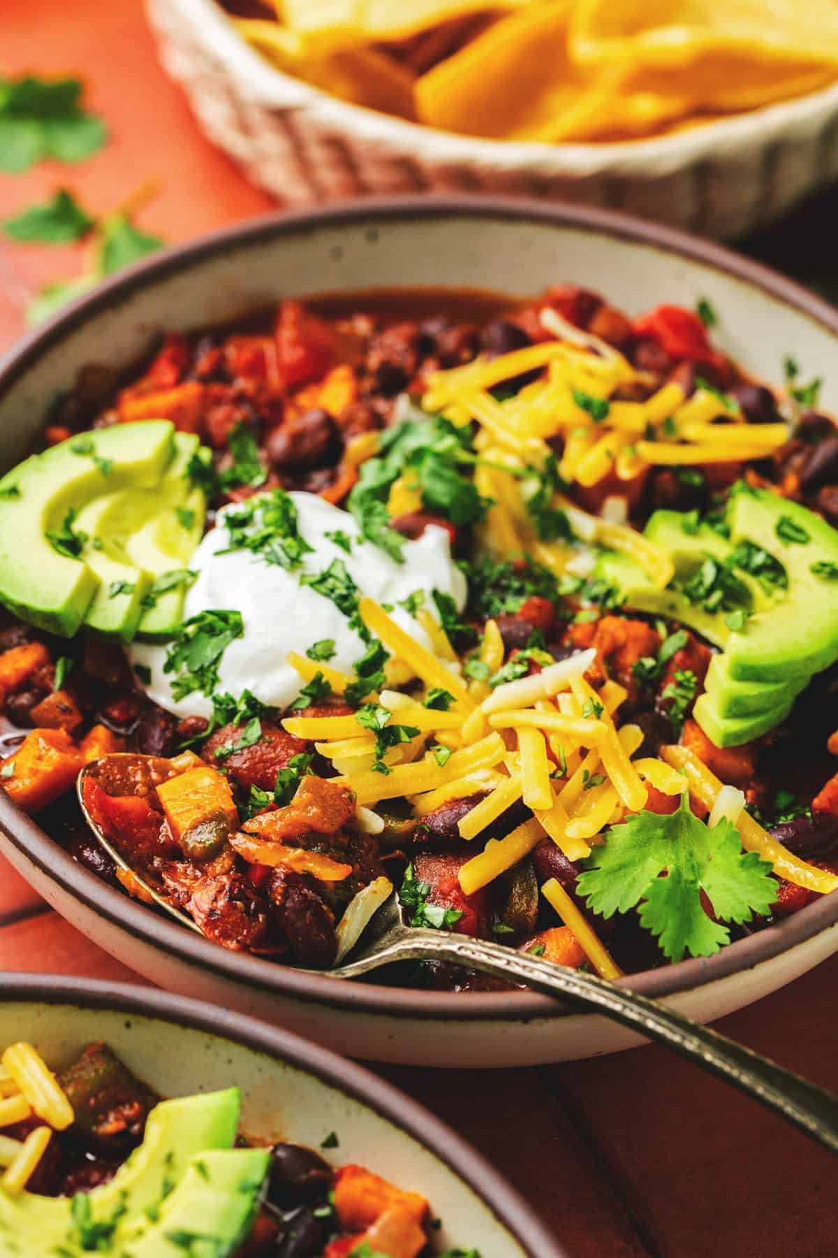 Spoon some chili into a bowl topped with cheese, avocado, and sour cream.