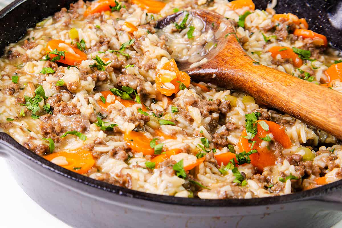 Skillet with burger and rice seasoned with parsley, close-up.