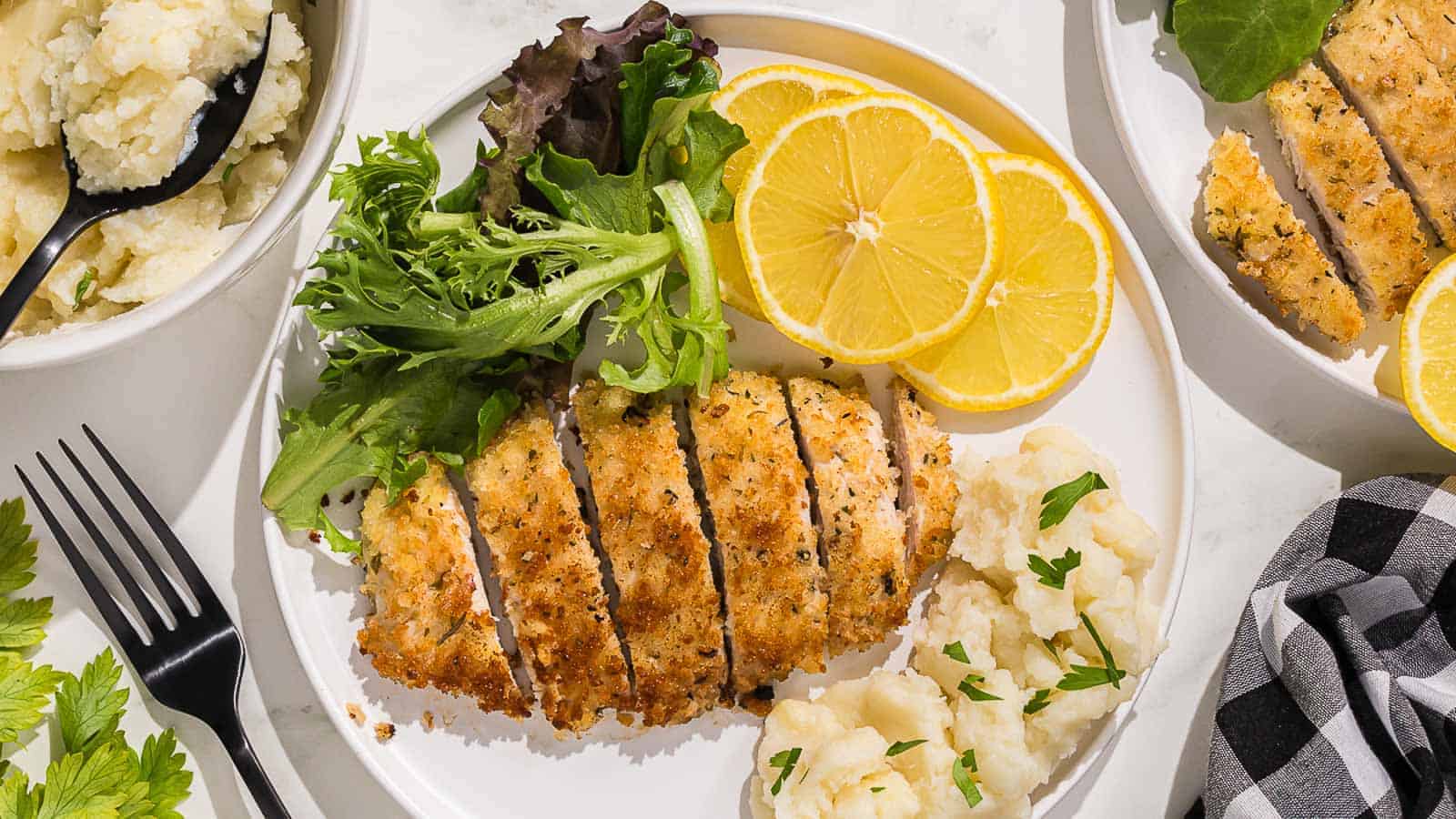 Breaded Italian chicken cutlets on a black plate with lemon slices.