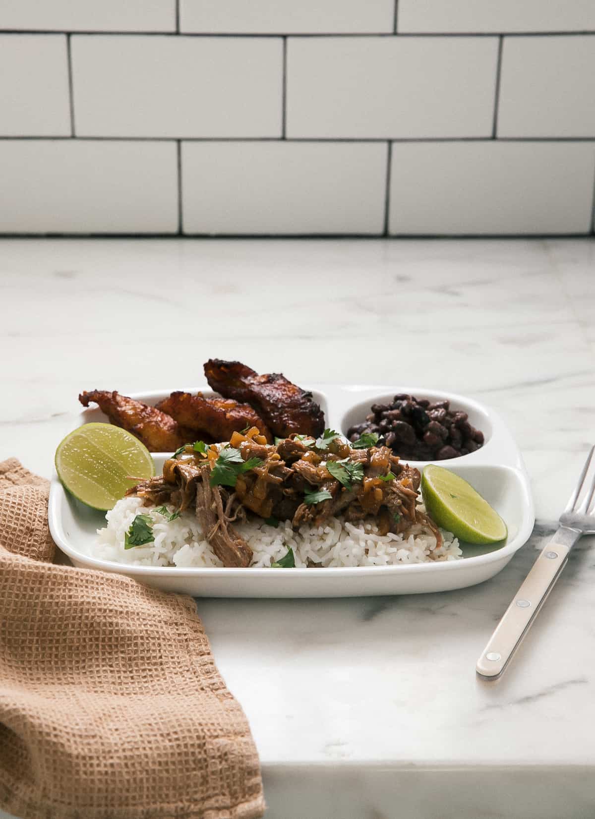 Direct view of Roasted Lechón directly on a plate with lemon wedges, rice and black beans.