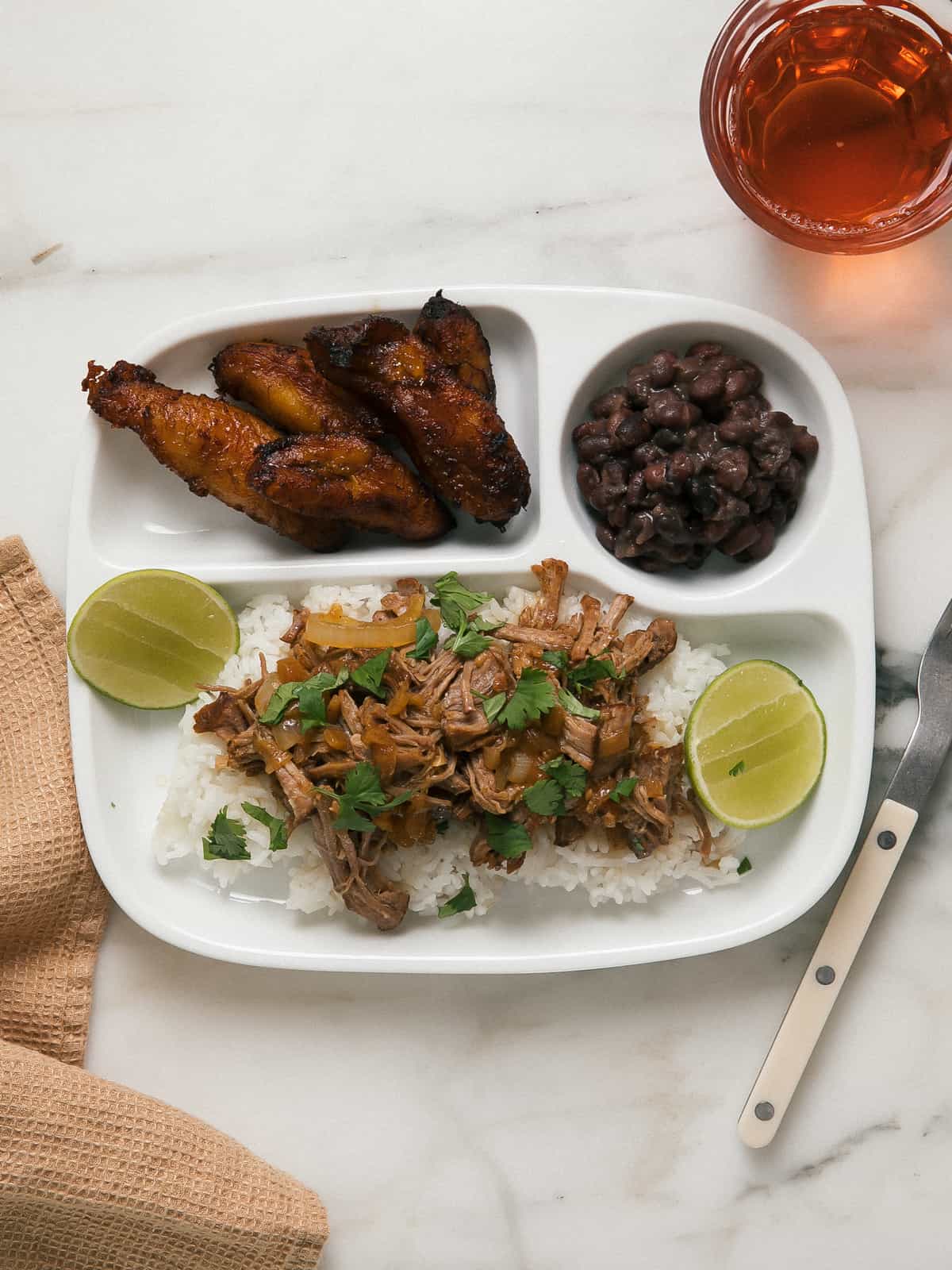 Overhead view of Roasted Lechón with fried plantains and black beans on a plate.