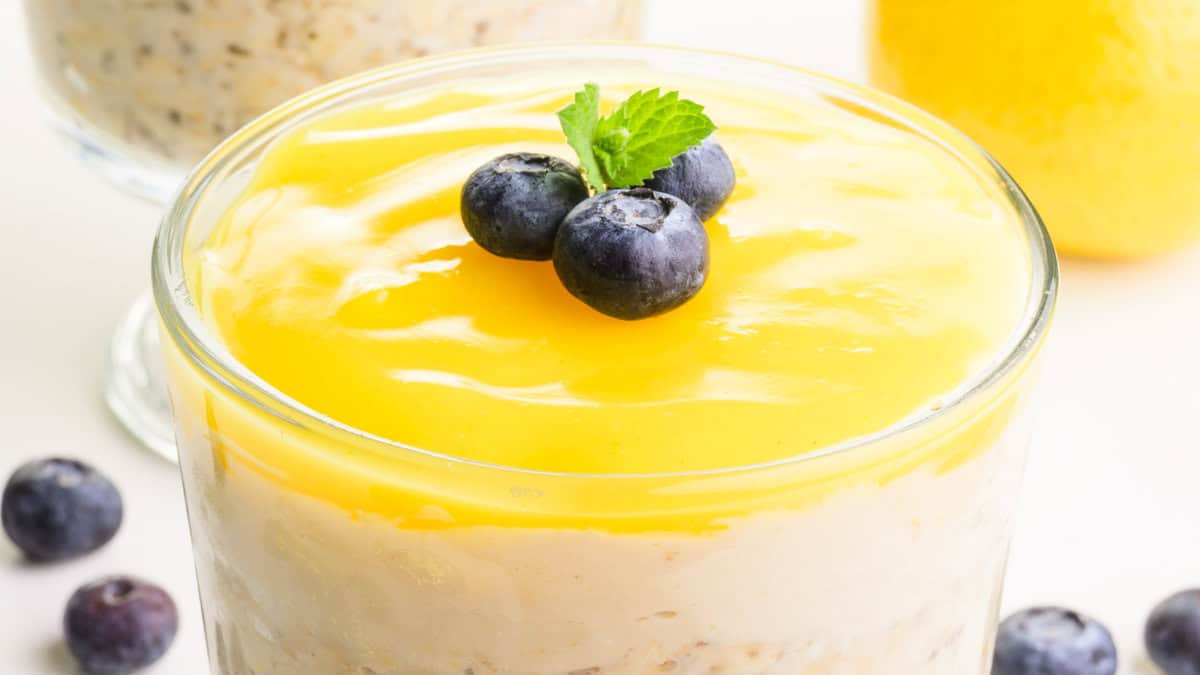 Close-up of a glass jar filled with layered oats. The oats appear yellow and include lemon slices and chia seeds.