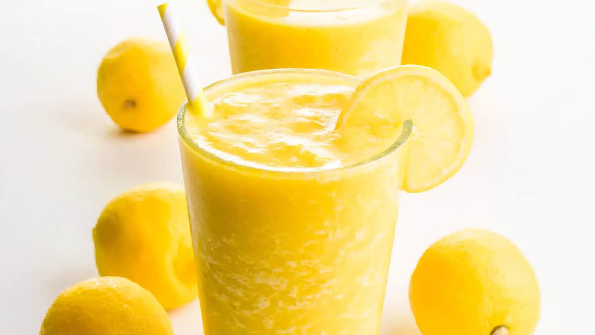 A close up image of a lemon smoothie with a lemon slice and a straw in class.