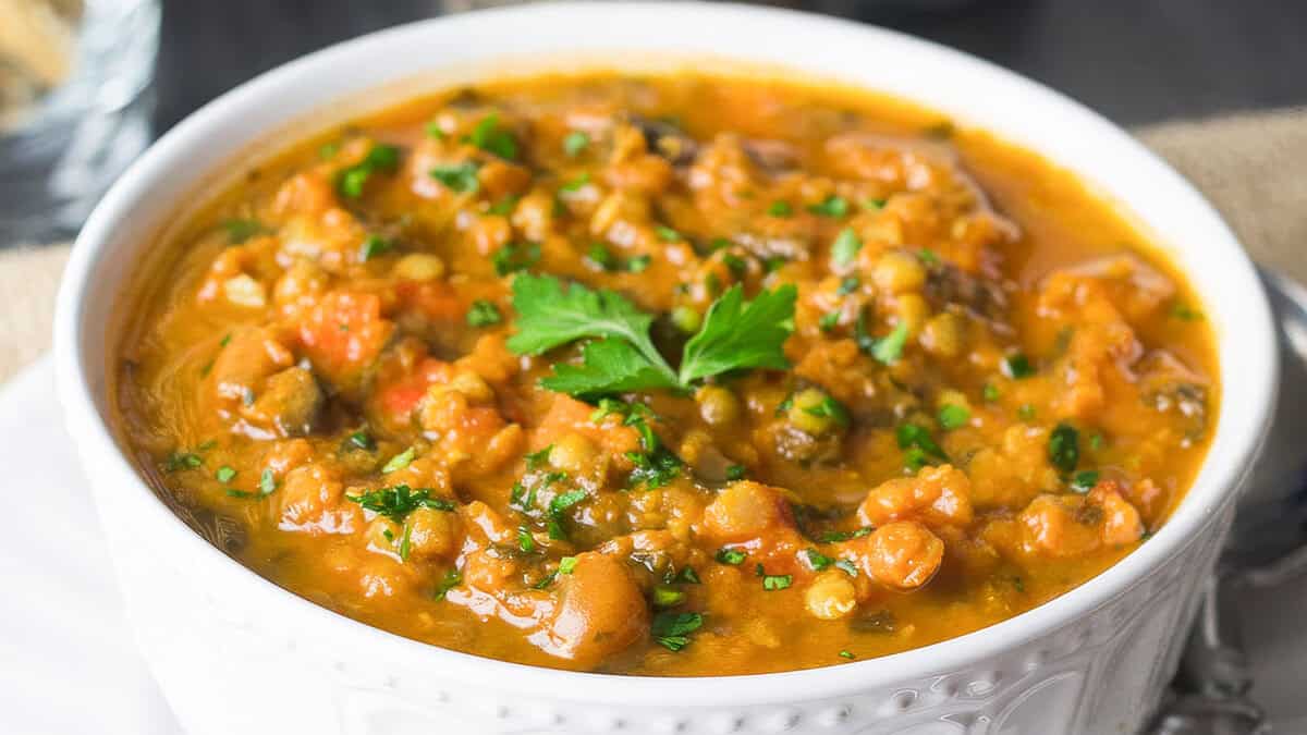 A close up image of lentil soup in a white bowl.