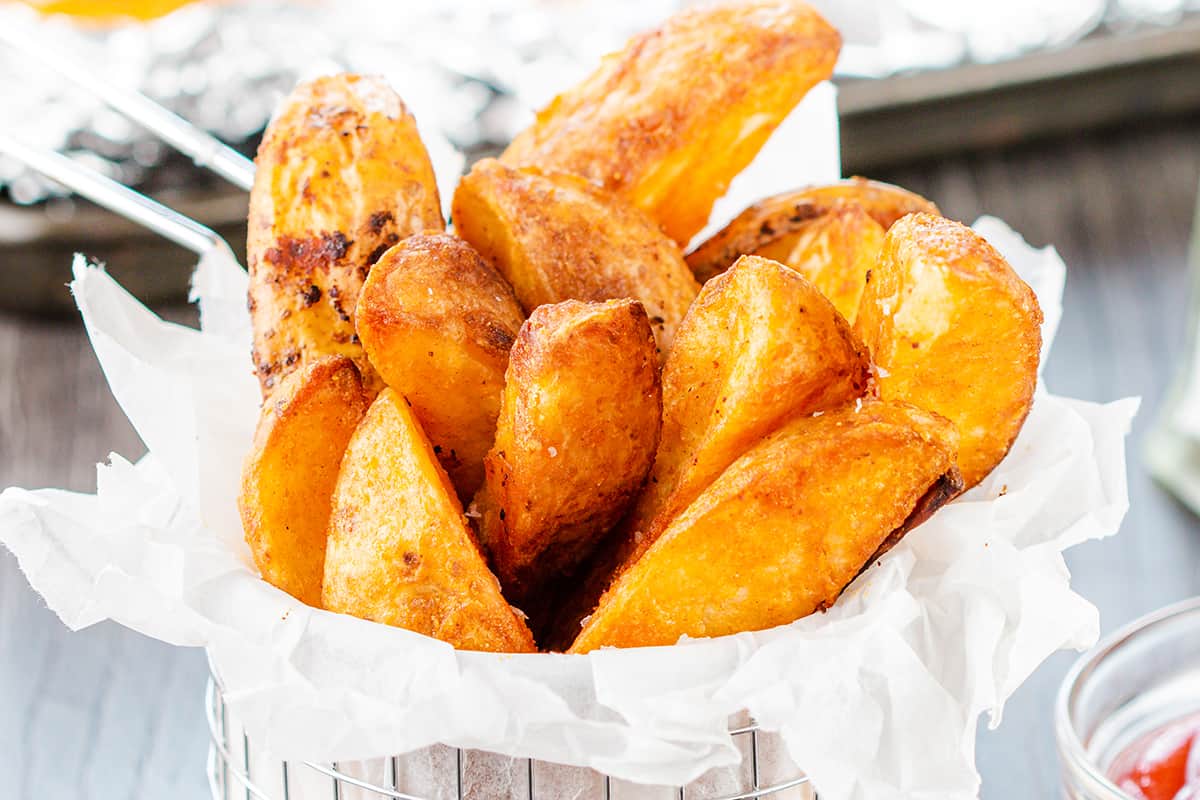 A metal basket filled with crispy, golden potato wedges.