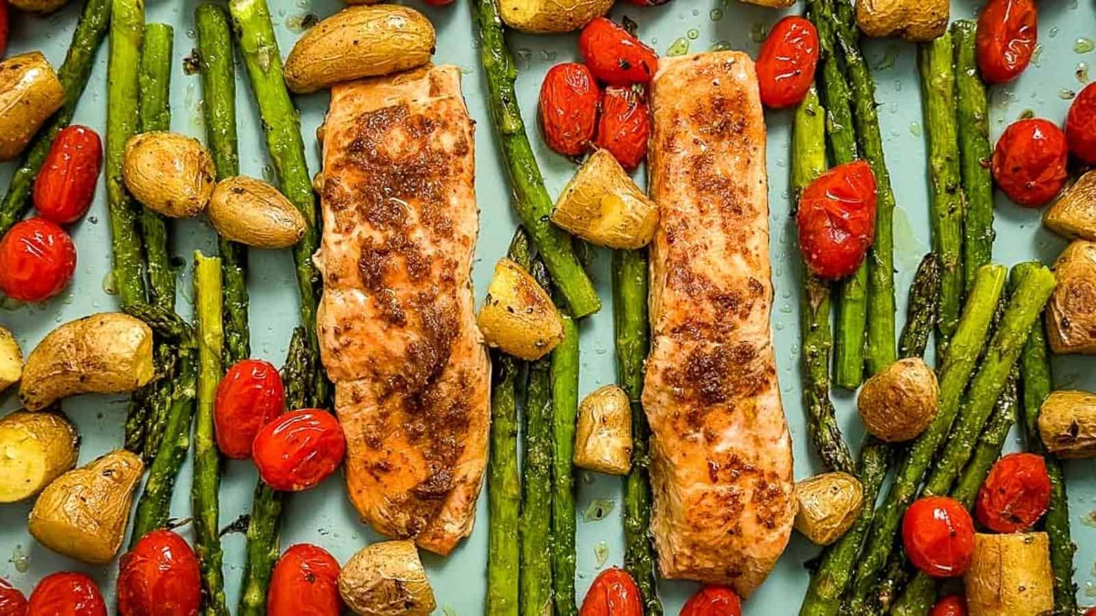 Close-up overhead view of grilled salmon, asparagus, baby potatoes and cherry tomatoes on a blue tray.