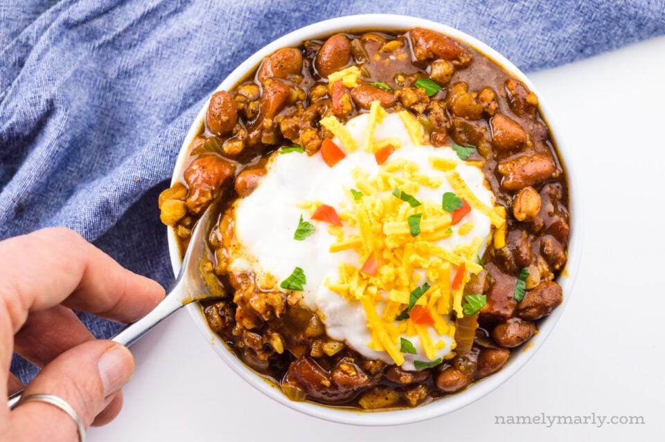 A hand holds a spoon dipping it into a bowl of vegan chili.