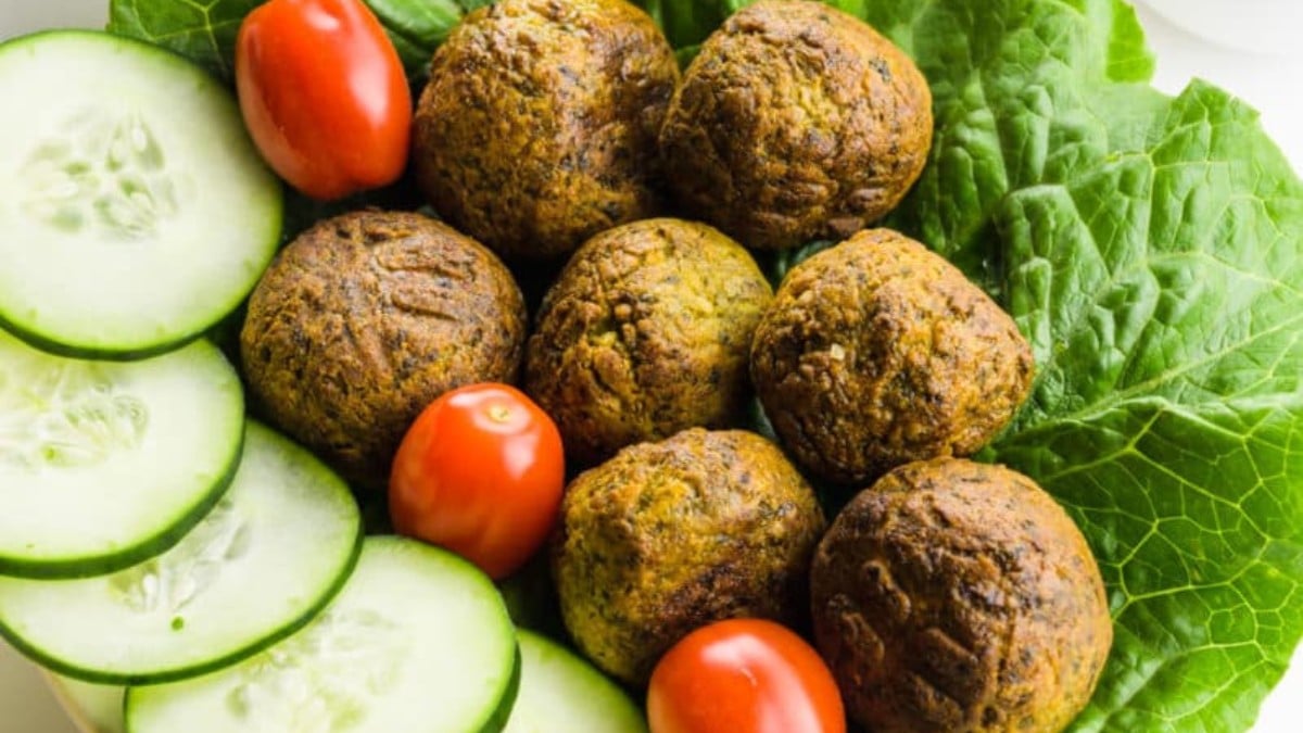 Several air-fried falafel balls rest on a bed of lettuce and are surrounded by vegetables such as cherry tomatoes and sliced ​​cucumbers.