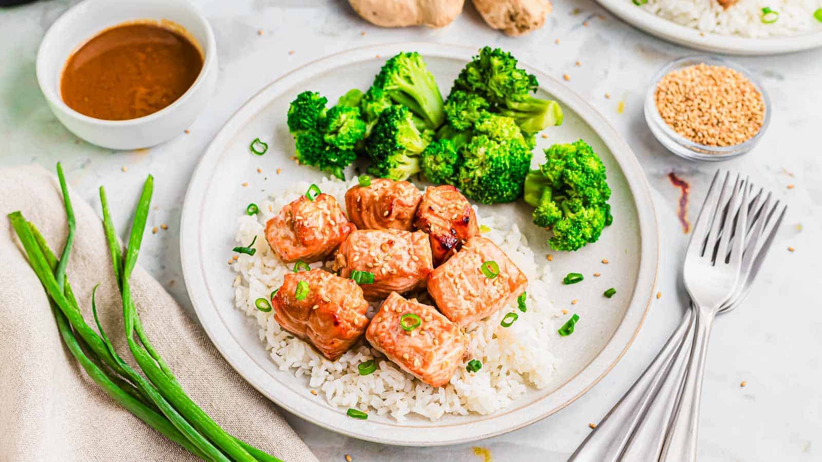 A plate with air-fried salmon bites, rice, broccoli and sauce on top.