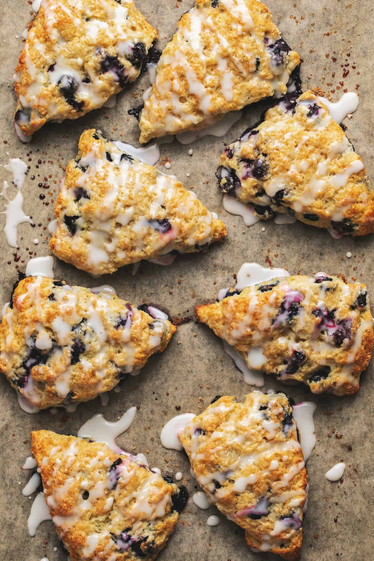 Overhead view of blueberry scones with frosting on parchment.