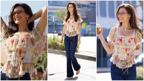 Bella Hadid's latest look reflects 2000s fashion with a modern twist. She wore a ruffled top embellished with a white floral print and a fitted corset, paired with bootcut jeans, clear glasses and chunky jewelry, exuding pure sass. (Instagram/@justjared)