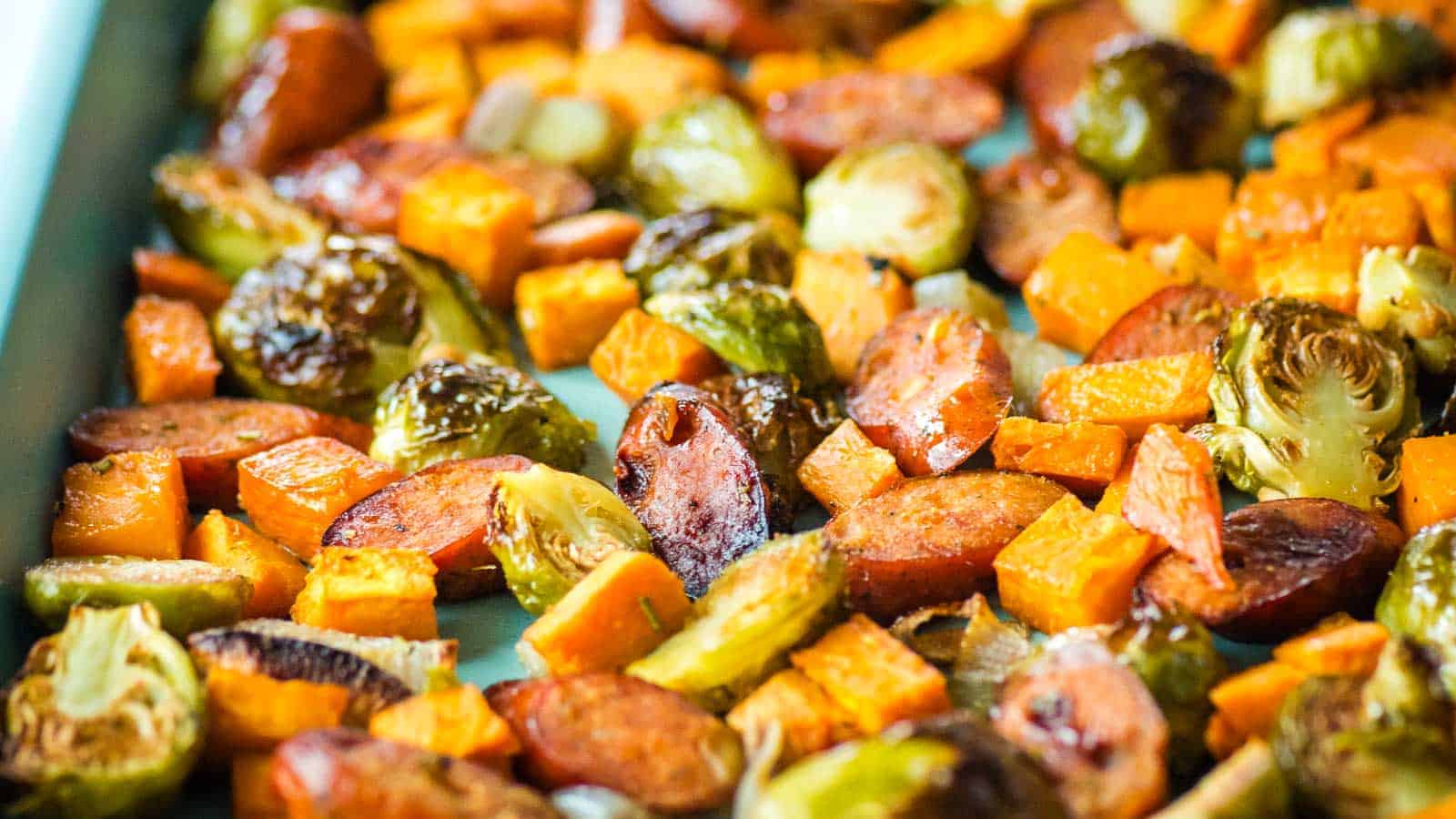 Roasted chicken sausage with apple, sweet potatoes, Brussels sprouts and shallots on a baking sheet.