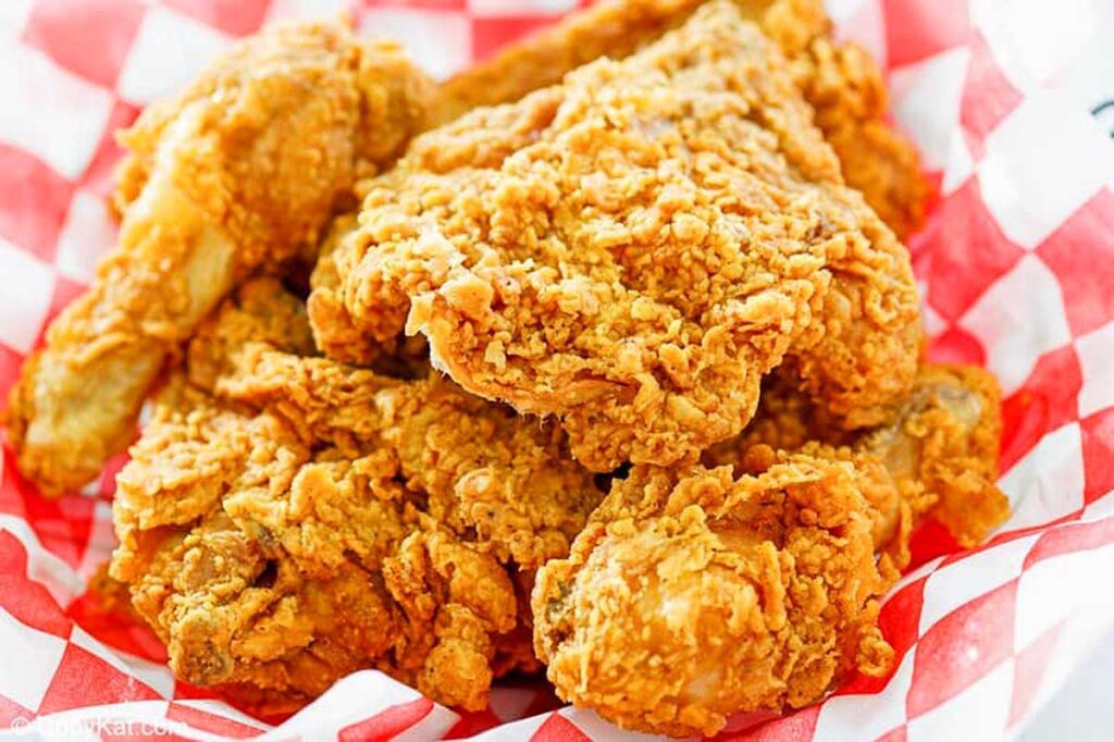 A basket of golden fried chicken on a red and white checkered napkin.