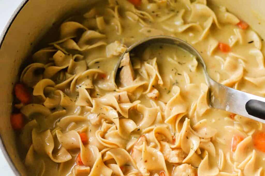 A pot of chicken noodle soup with a ladle resting on the edge.