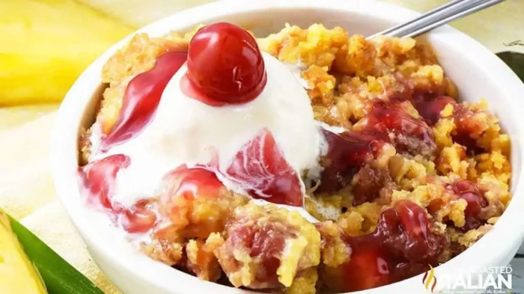 A close up image of a pineapple cherry cake topped with whipped cream and a cherry.