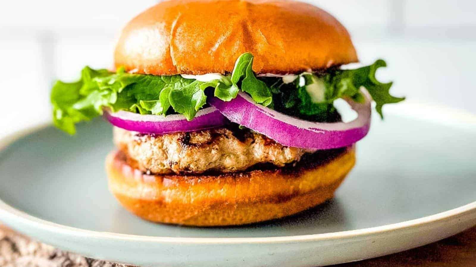 A close-up side view of an air fryer turkey burger is shown on a light blue plate.