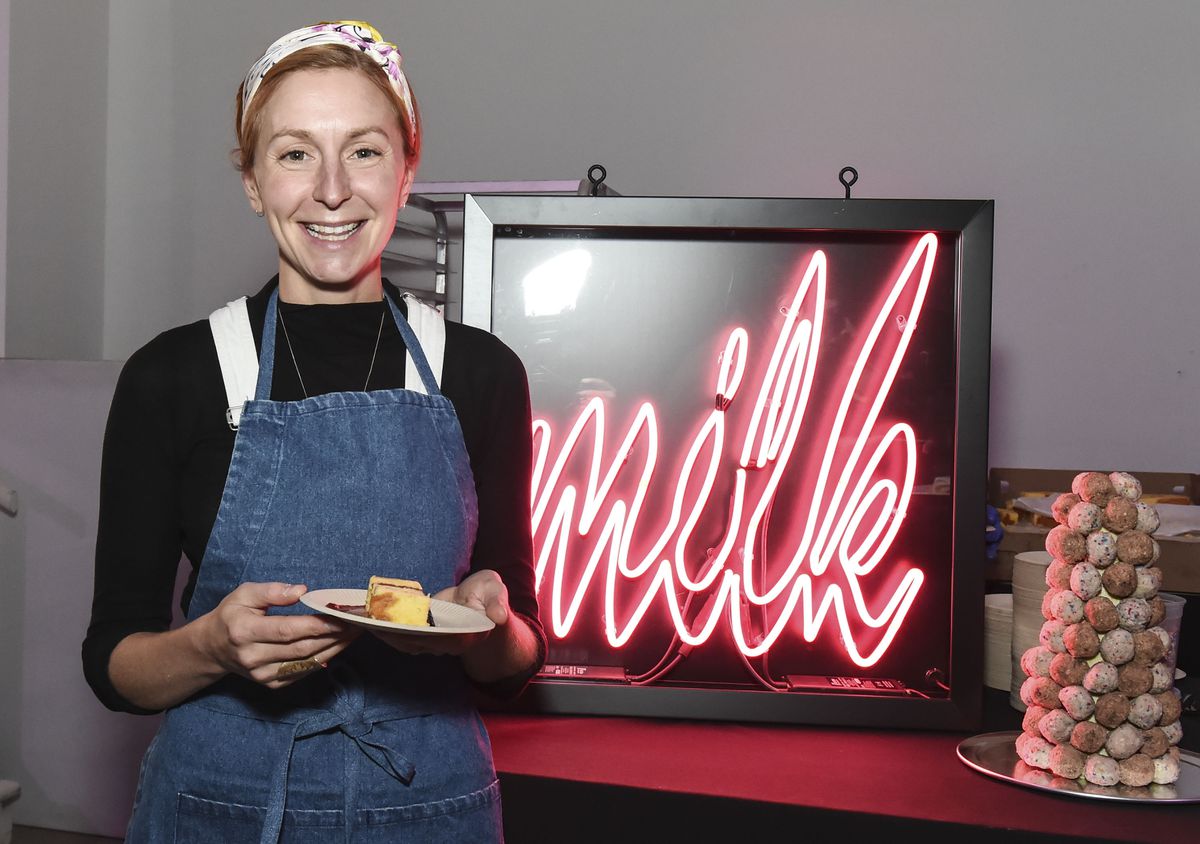 Chef Christina Tosi poses with a slice of cake in front of a neon sign that reads 