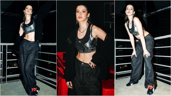 Shanaya Kapoor looked chic in a Puma bralette with shiny silver detailing. She paired it with black baggy trousers and a matching jacket, and elevated the ensemble with trendy sneakers and oversized silver jewellery. (Instagram)