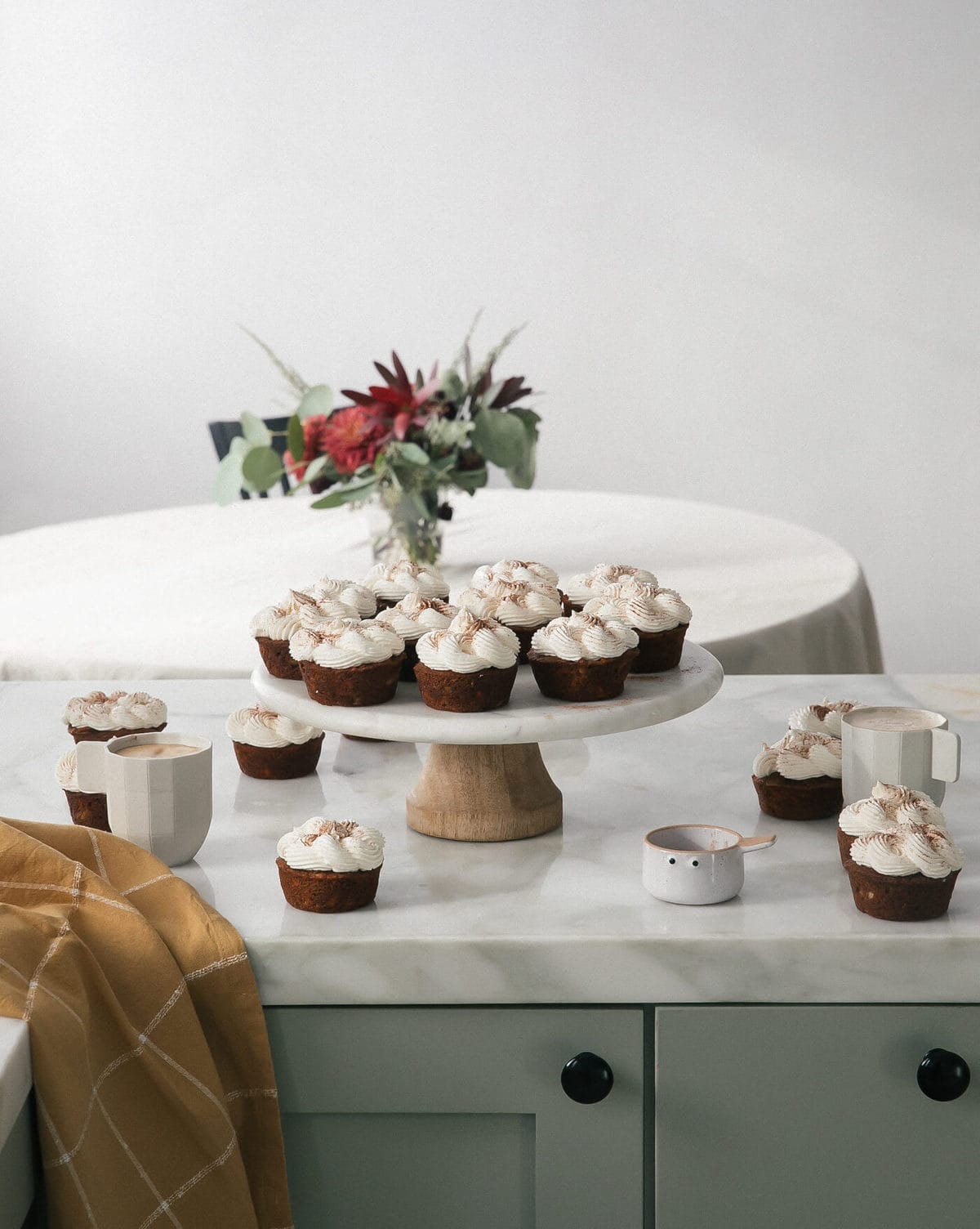 Carrot chai cupcakes frosted with spiced maple frosting on the counter and on a cake stand.