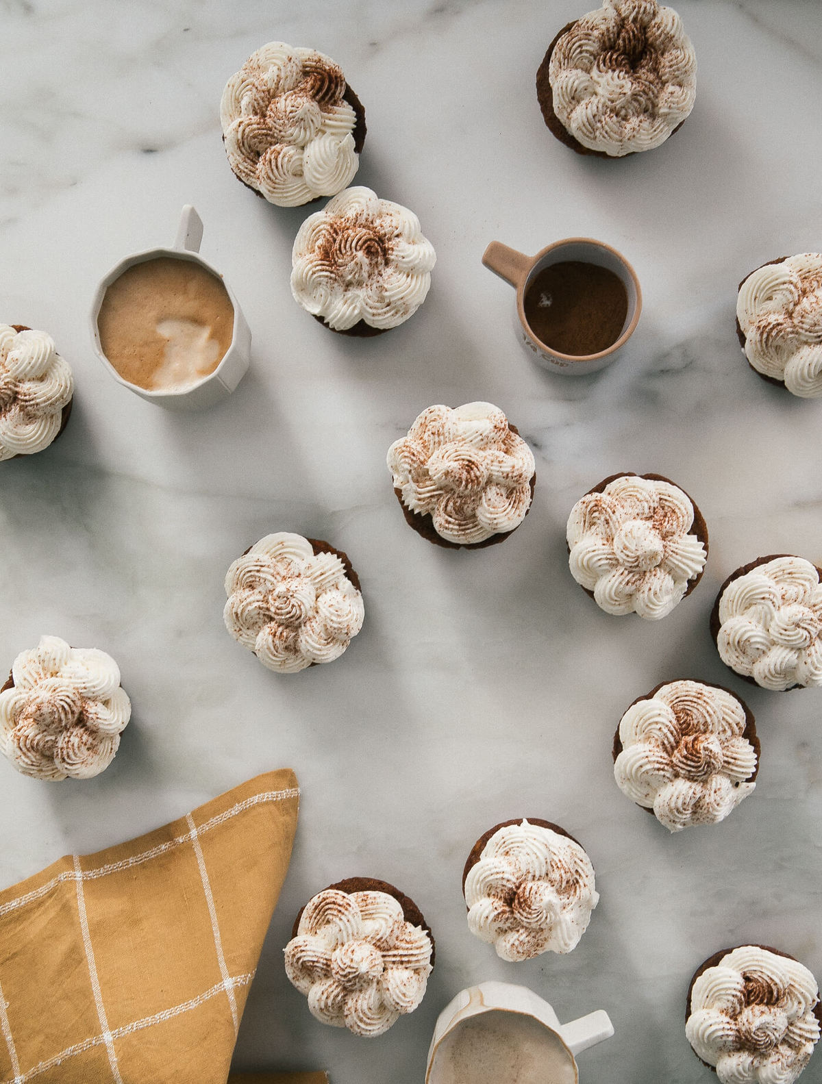 Overhead view of carrot chai cupcakes with spiced maple frosting on a counter with coffee cups.