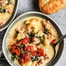 A bowl of zuppa toscana topped with bacon next to a baguette