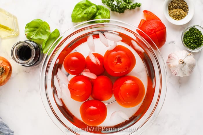 Tomatoes in a cold bath with ingredients around them to make fresh tomato sauce