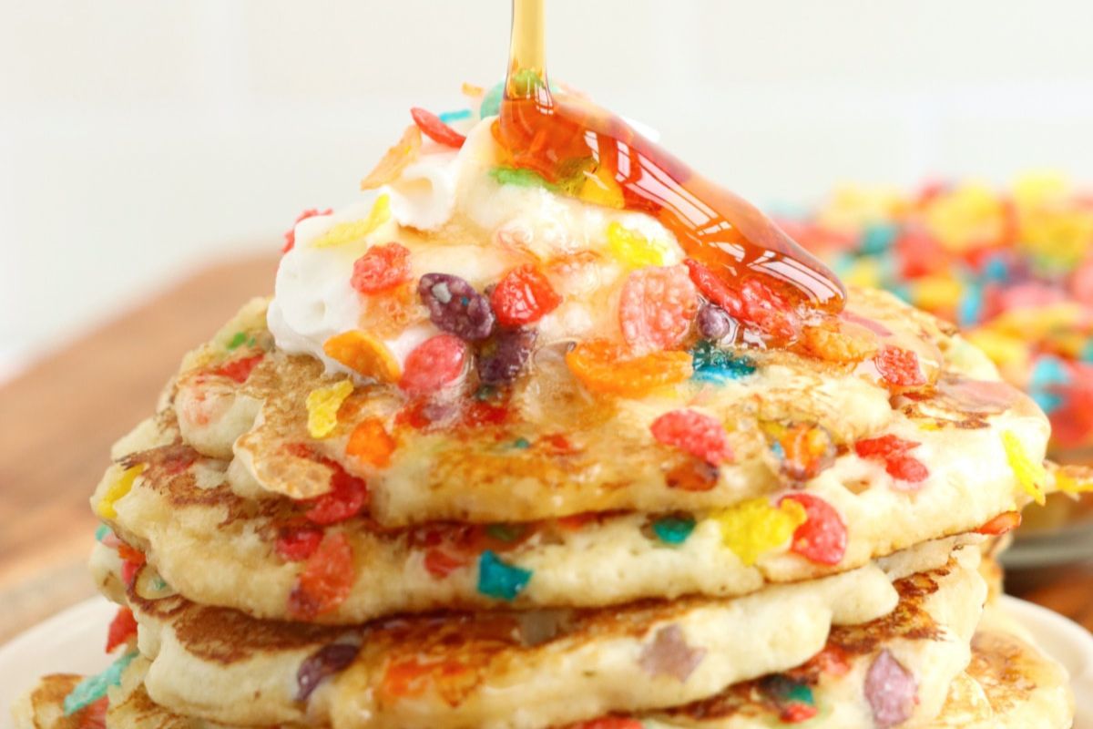 A stack of pancake recipes pancakes with colorful cereal pieces and syrup poured on top.