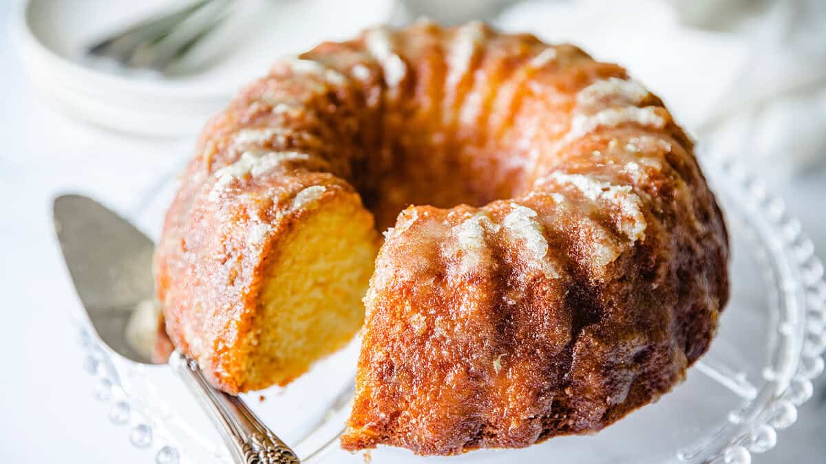 An orange Bundt cake on a glass stand.