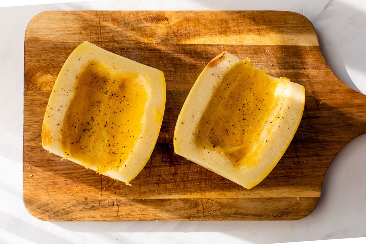 Two halves of spaghetti squash on a cutting board with the insides scooped out