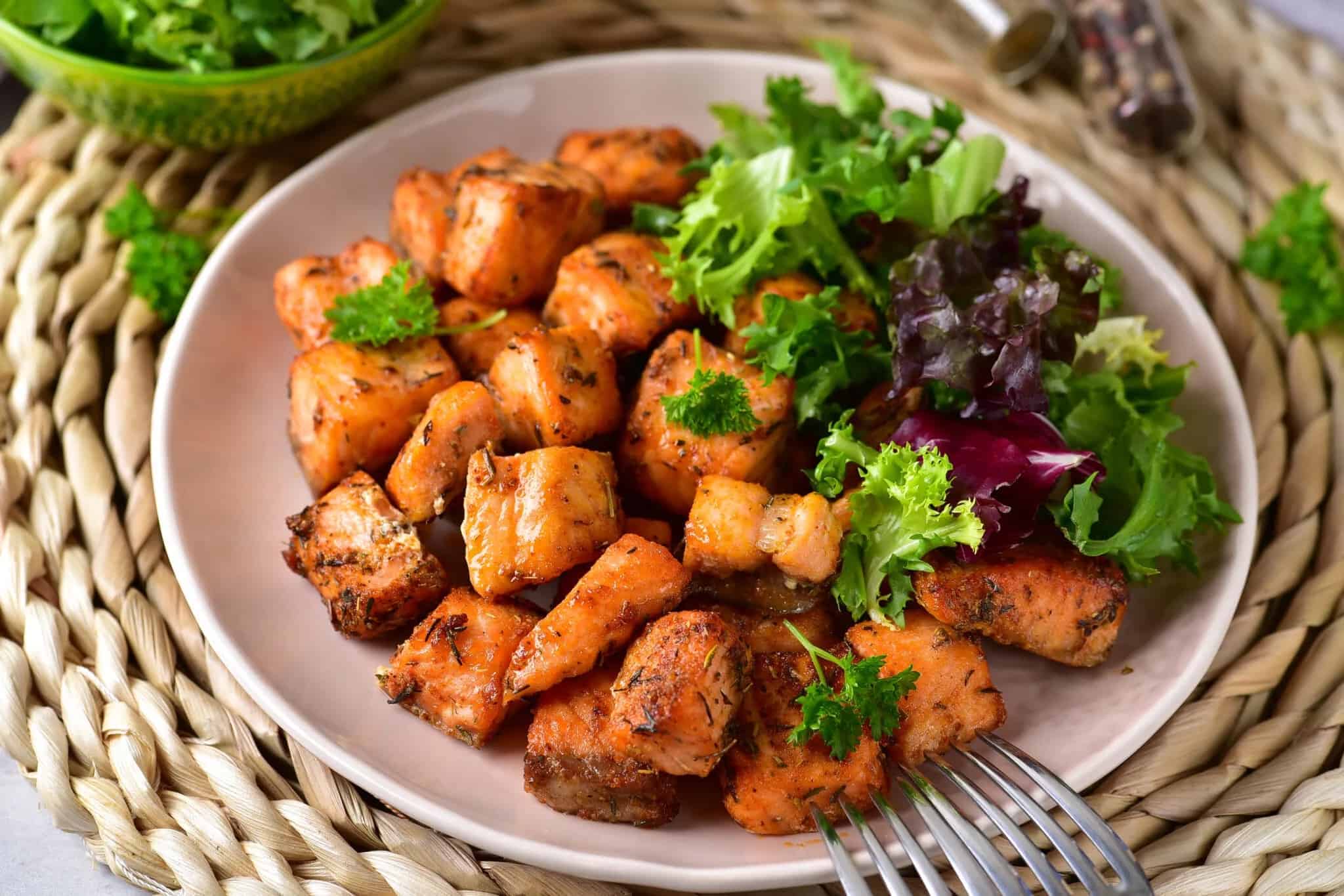 Air fryer salmon bites and salad on a plate with a fork.