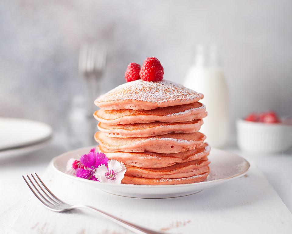 A stack of raspberry pancakes sprinkled with powdered sugar.