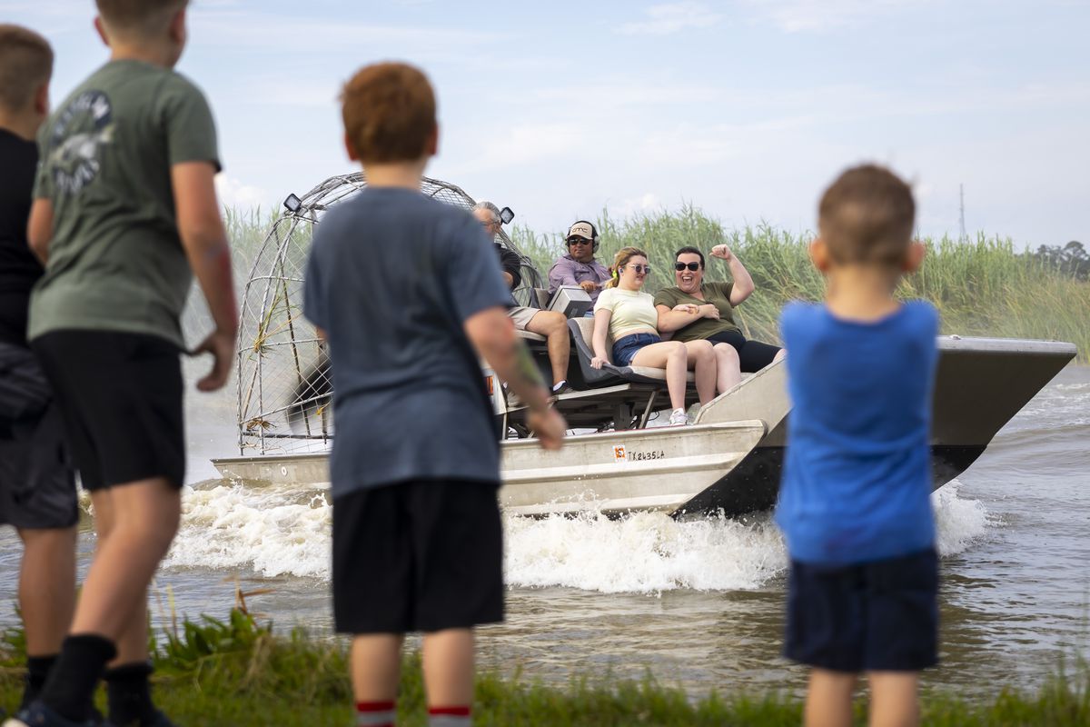 Airboat passengers cheer as they pass by children on the shore at Texas GATORFEST in Anahuac.